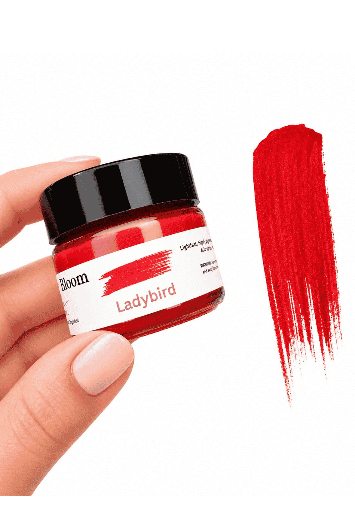 Jar of red paint labeled 'Ladybird' held by a hand with a swatch of red paint on a white background.