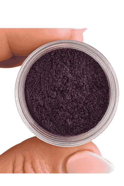 Small container of dark purple powder held by a hand on a white background