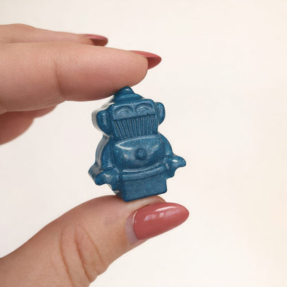Hand holding a small green blue decorative item against a plain background
