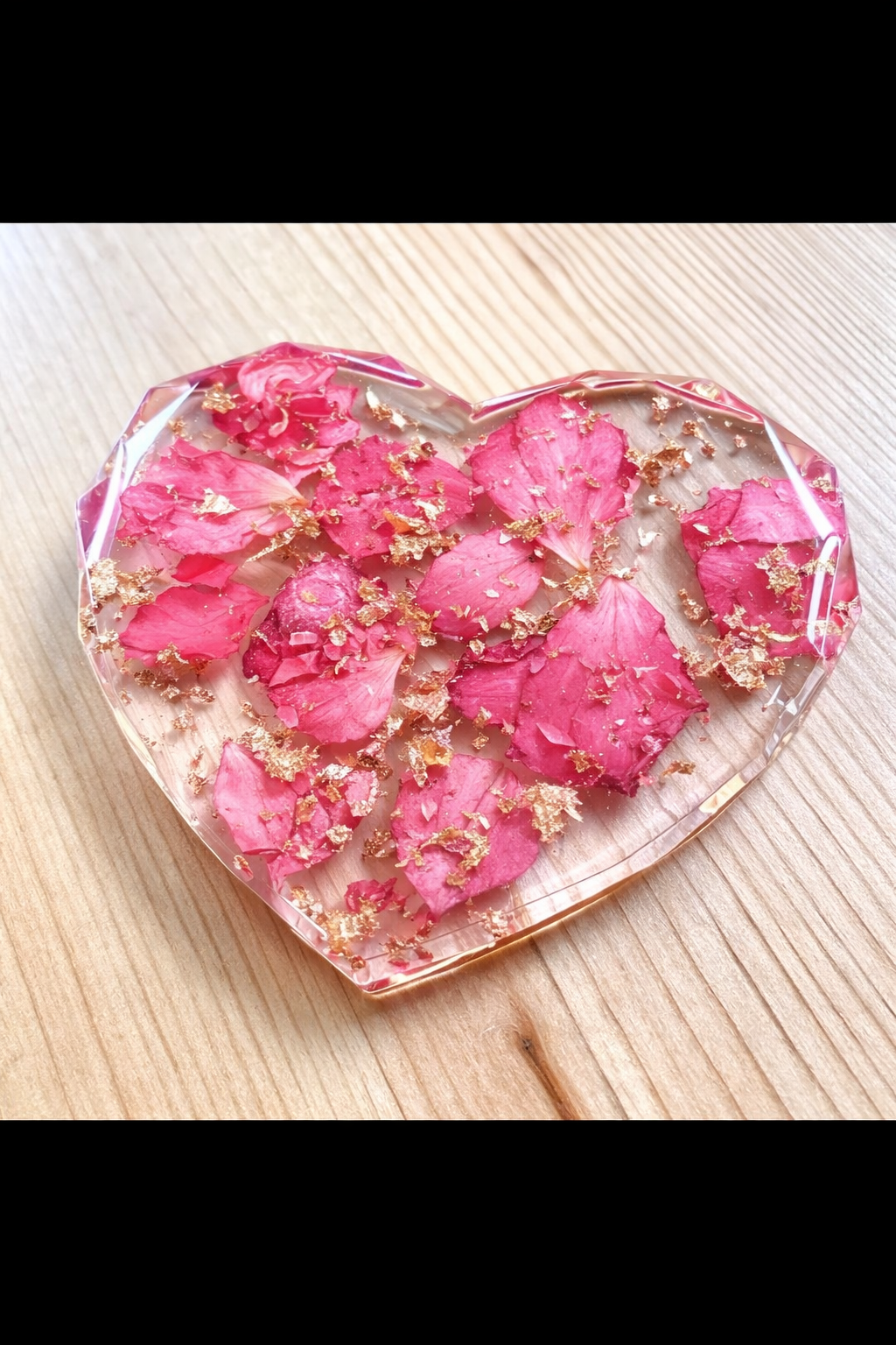 Heart-shaped resin coaster with pink floral petals on a wooden surface