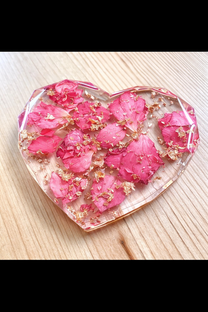 Heart-shaped resin coaster with pink floral petals on a wooden surface
