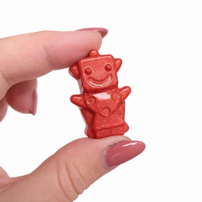 Red robot-shaped candy held between fingers against a white background