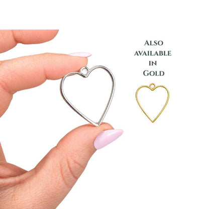 Gold and Silver heart-shaped open bezel charm held between fingertips with pale pink nails, photographed on a clean white background with soft natural lighting. Minimalist jewellery bezel ideal for resin crafts, UV resin pendants, shaker charms, and handmade jewellery making.