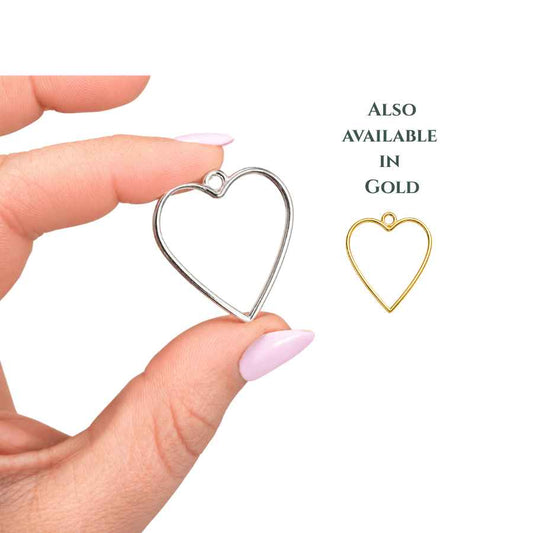 Gold and Silver heart-shaped open bezel charm held between fingertips with pale pink nails, photographed on a clean white background with soft natural lighting. Minimalist jewellery bezel ideal for resin crafts, UV resin pendants, shaker charms, and handmade jewellery making.