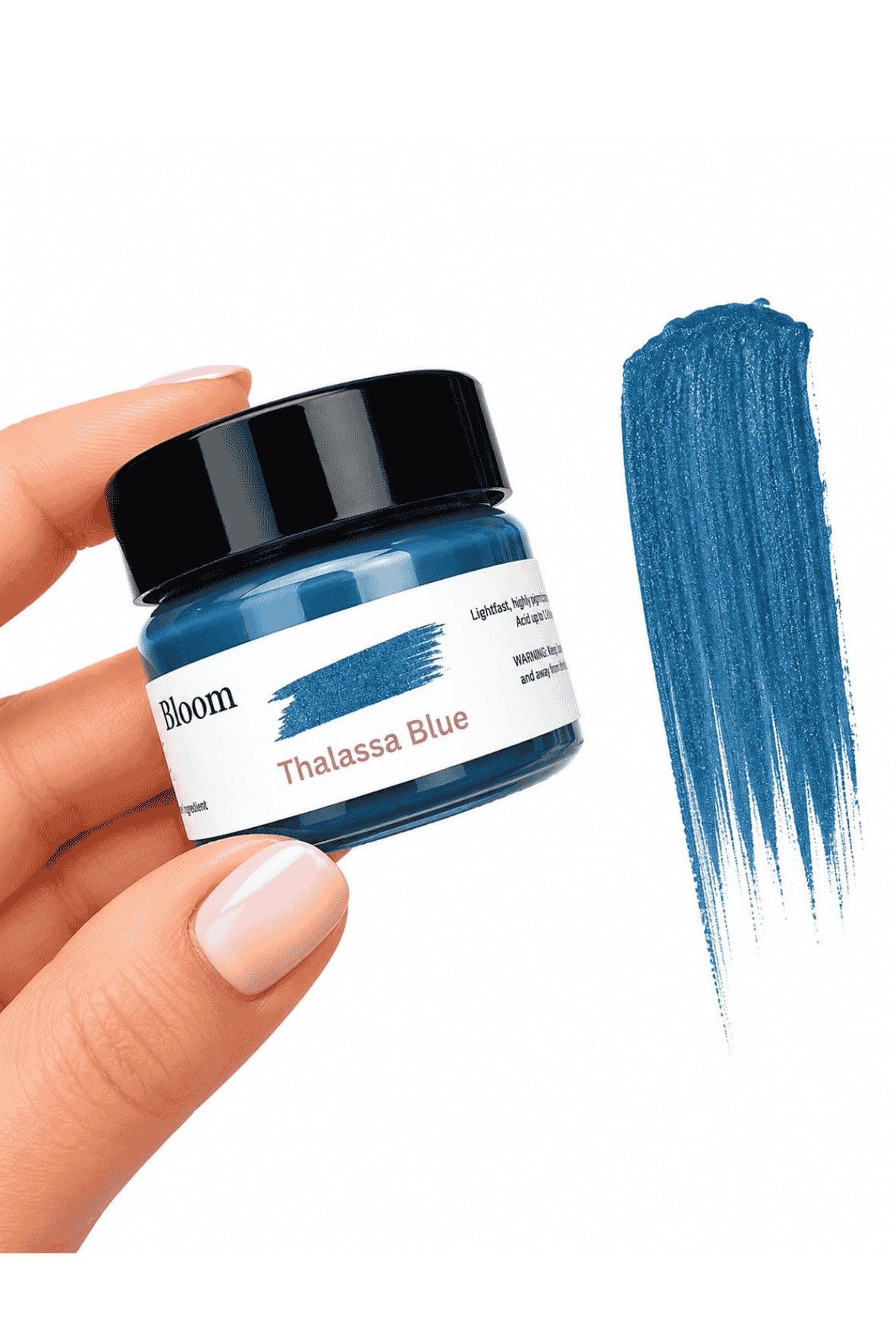 Jar of 'Bloom Thalassa Blue' paint held by a hand with a swatch of blue paint on a white background.