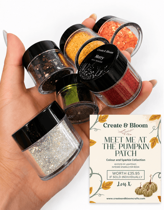 A hand holds six small jars of glitter and sparkles in various colors, including orange, red, green, silver, and black. A printed card for the 'Create & Bloom Meet Me at the Pumpkin Patch' collection is shown in the lower right corner on a white background. chameleon aurora sparkle collection, special glitter for resin, autumn glitter colours for mixed media and homewares. Glitter for resin, glitter for epoxy