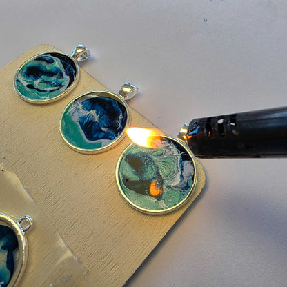 Using a flame to pop surface bubbles on ocean-inspired resin necklace pendants