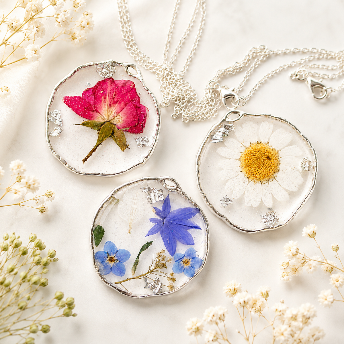 Three finished pressed flower resin necklaces in silver coloured pendant bezels